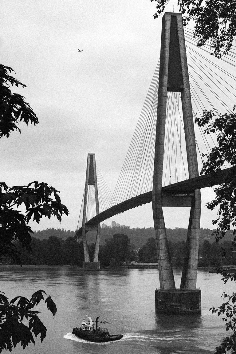 A view across the Fraser River with a bridge, plane and tugboat.