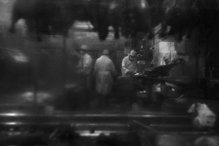Three butchers observed through a greasy shop window.