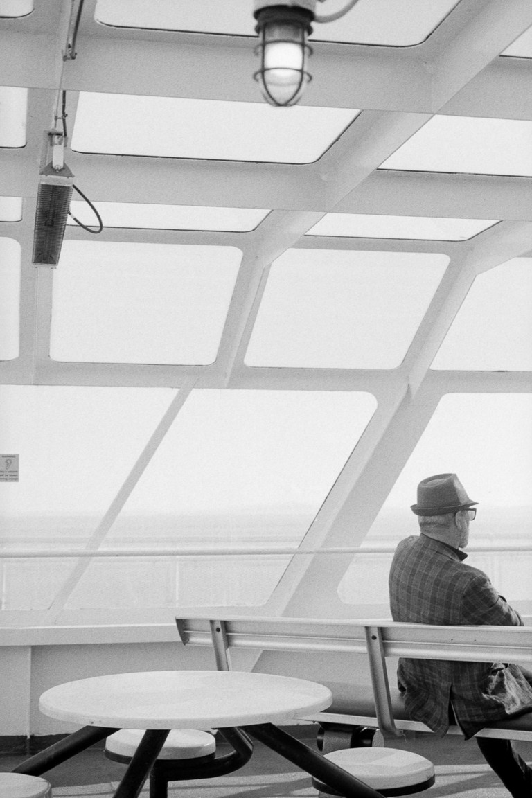 A man with folded arms glancing out into the ocean as he passing the time under sail. 