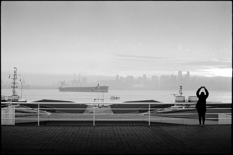 A person holds their phone aloft to attempt to capture the harbour and city scape.