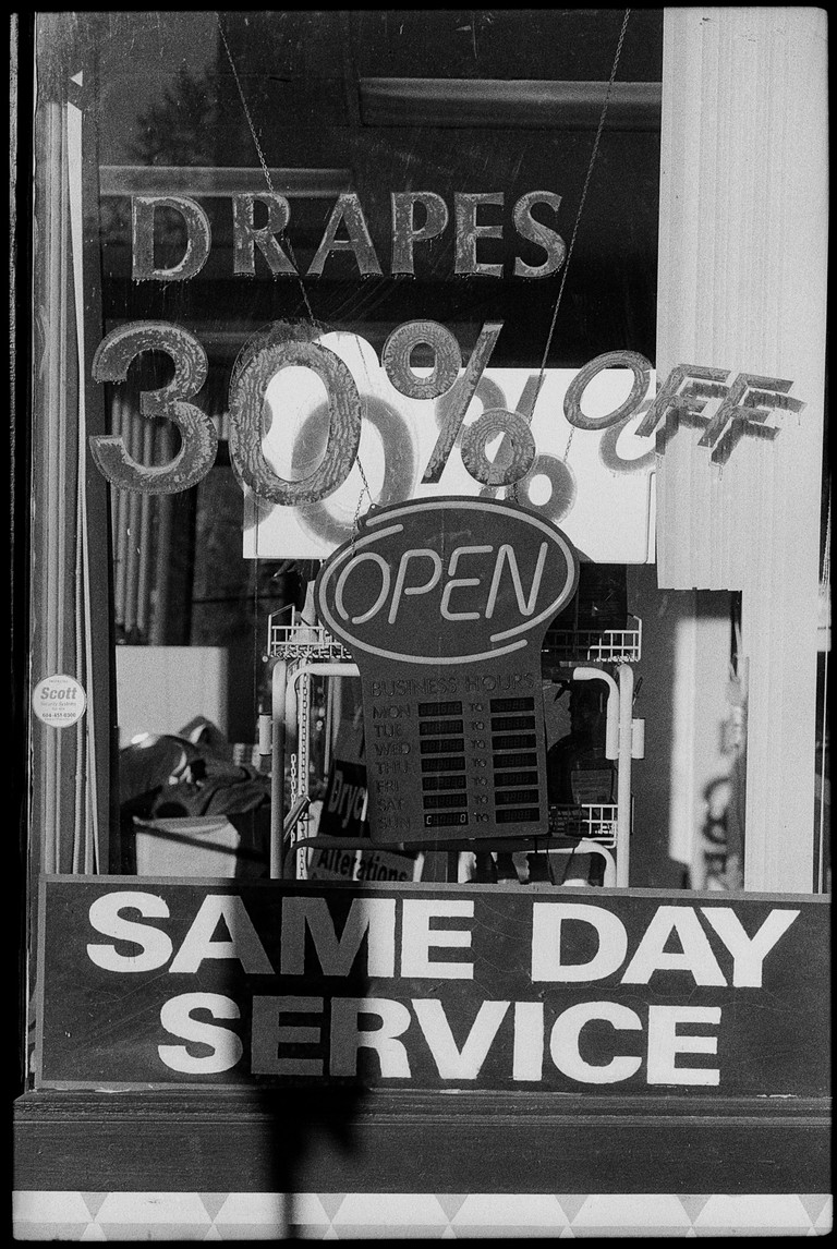 A dry cleaning shop window festooned with chaotic lettering, many of the letters castings shadows on the surfaces behind them..