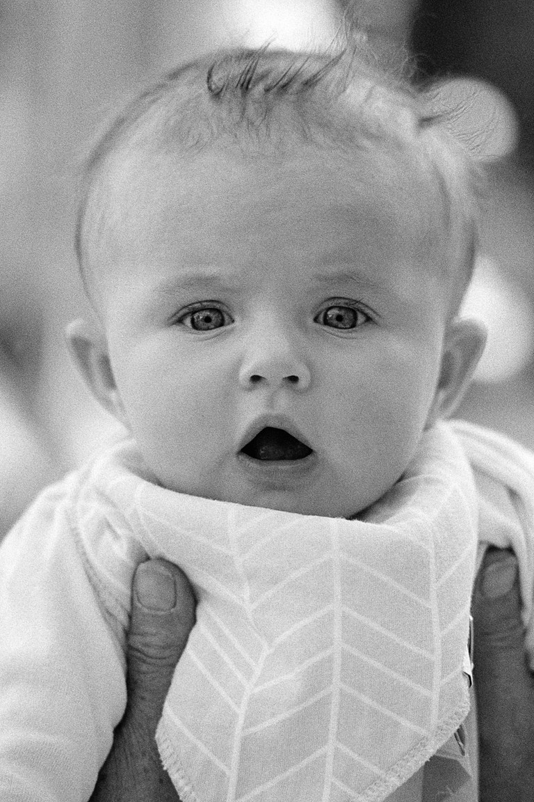 An infant gazes intently while being held aloft by weathered hands.