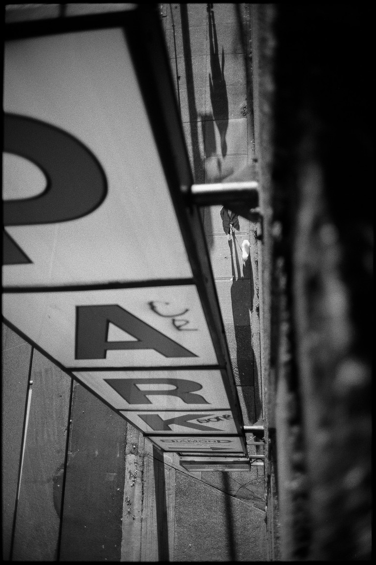 A woman walks a small dog under looming sign that says 