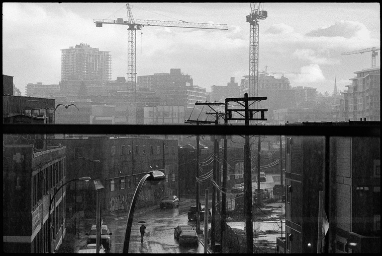 The sun lights a street slick with the rain. Part of the sky clears while rest crashes down on a loan pedestrian hiding beneath his umbrella.