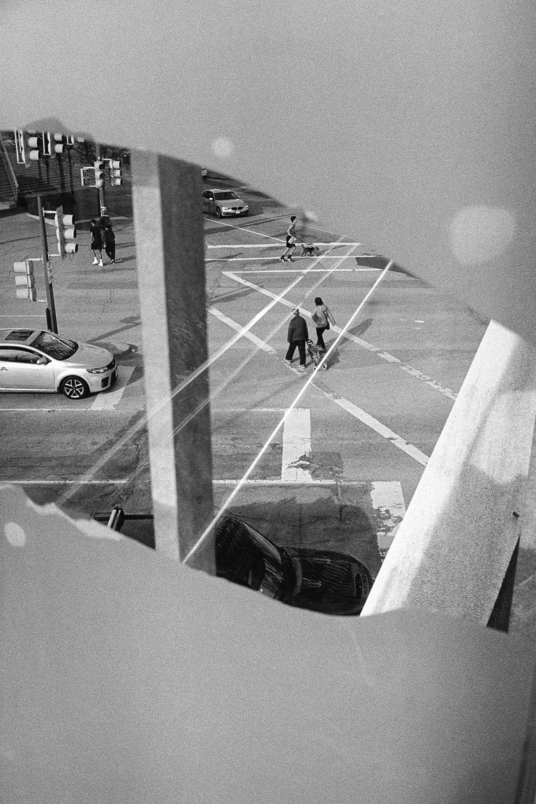 Pedestrians navigate a geometric maze of lines, vehicles and reflections.