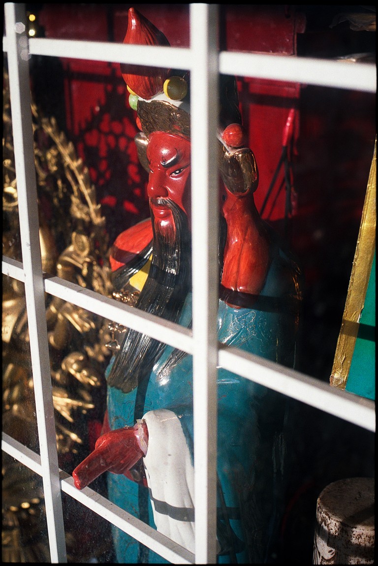 A statue behind a shop window seems to flirt with the boundaries of the shop by sticking its fingers out through the security bars.