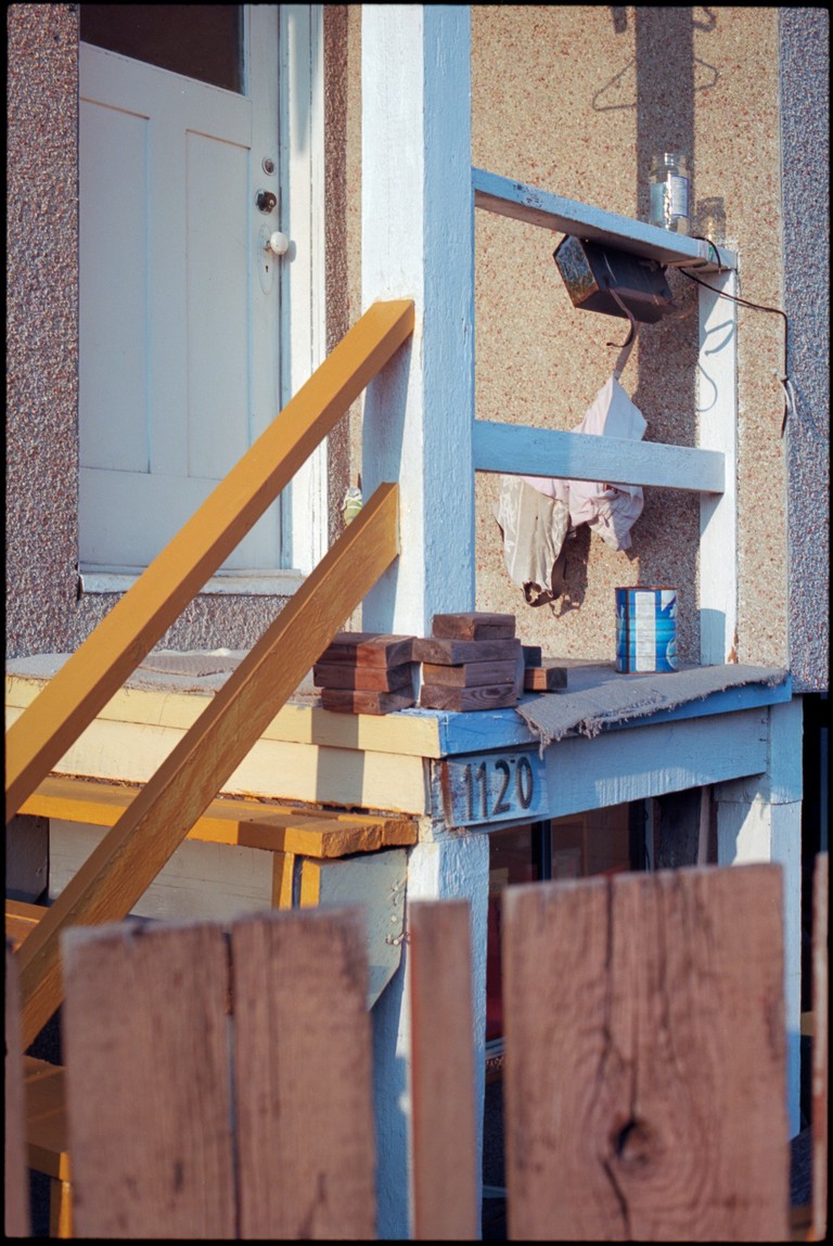 An staired entrance to a home exhibits an eclectic and random level of clutter and appears to have been painted with an almost child's naivety.
