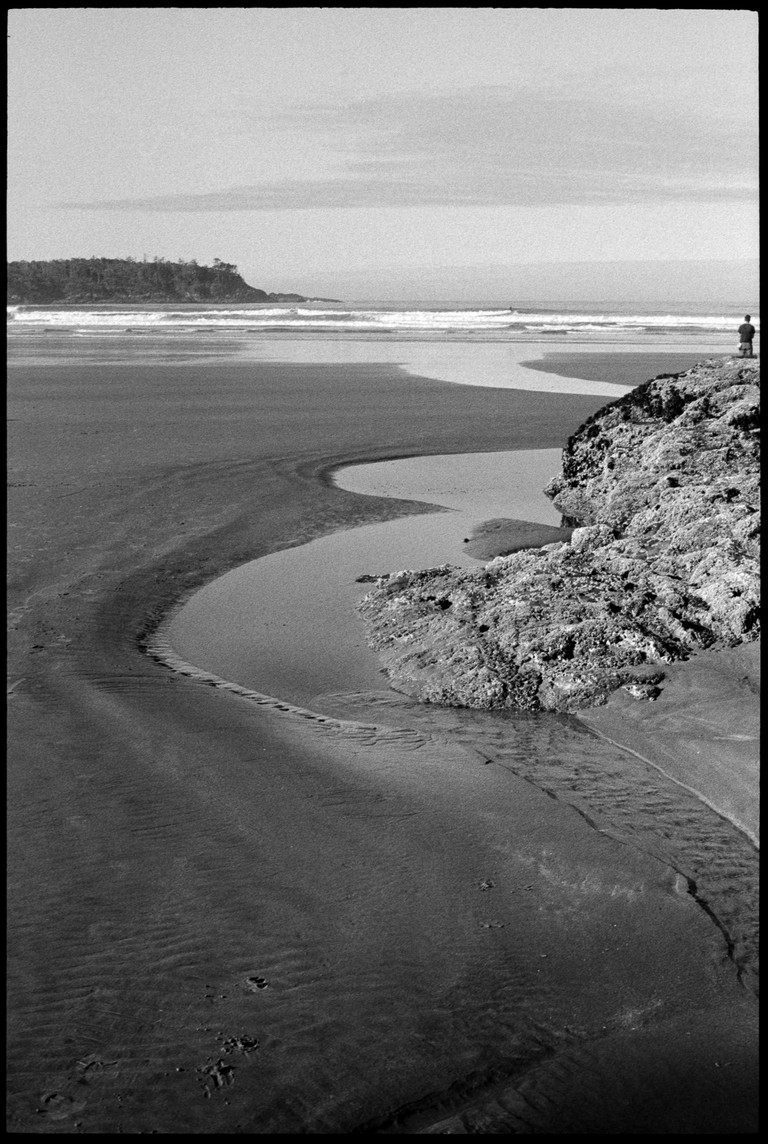 A stream meanders around some rocks to the the ocean.