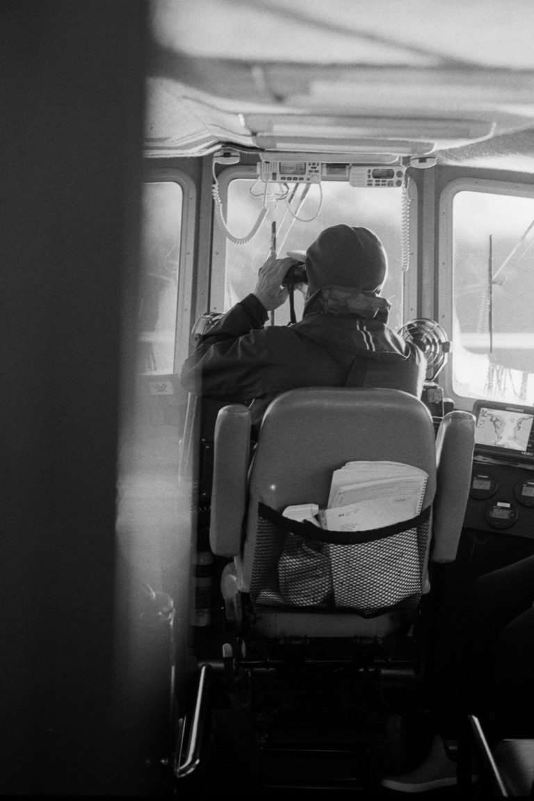 A captain scans the scene from the bridge with binoculars.