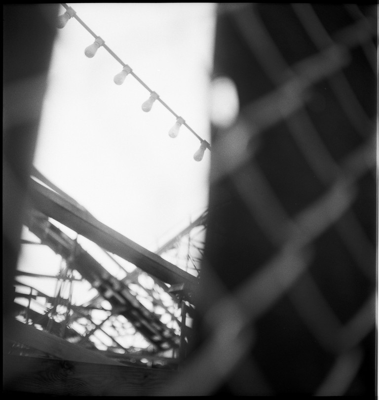The layered structures of a wooden rollercoaster as seen through a tear in a blind. 