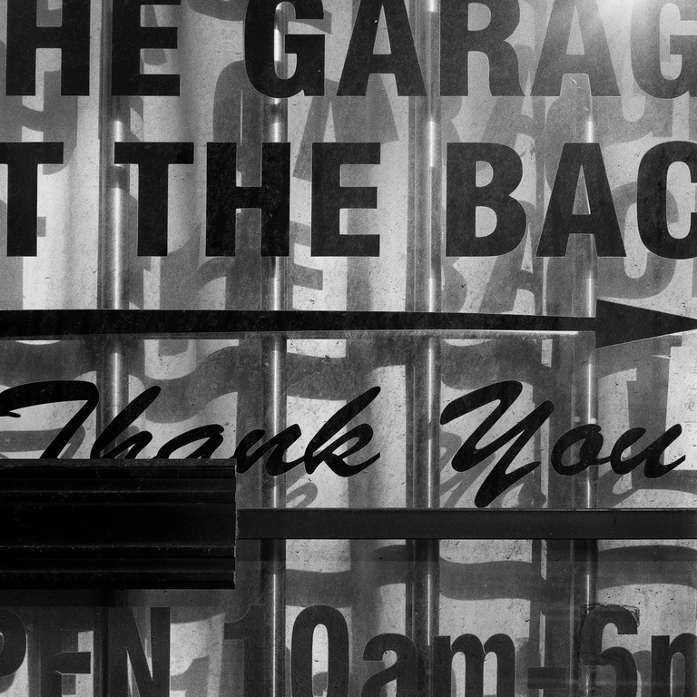 Detail of an automotive shop window, with the shadows of the letters stating hours cast on a flowing curtain.