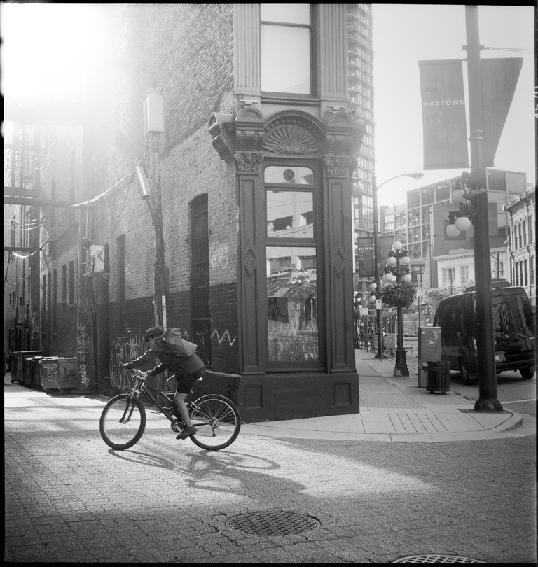 A lone person rides down a sunlit Gastown alley.
