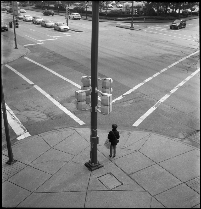 A pedestrian waits at a busy crossing. The traffic seems almost eerily organized.