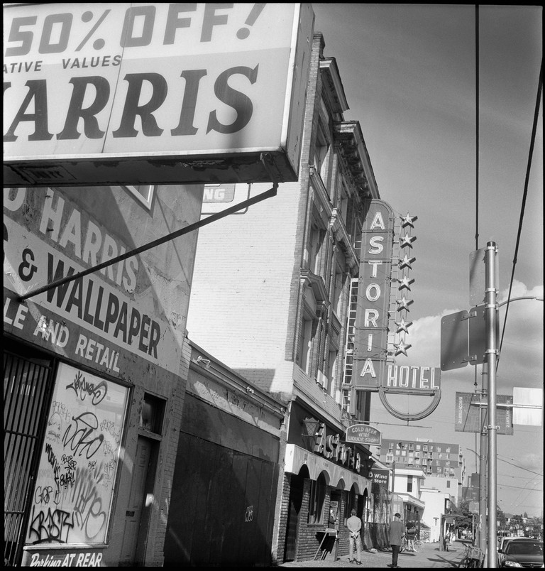 Pedestrians lazily proceed down a block festooned with neon signs and graffiti. 