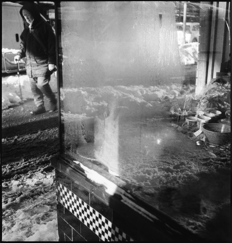 A woman carefully navigates the sidewalk in front of a shop window. 